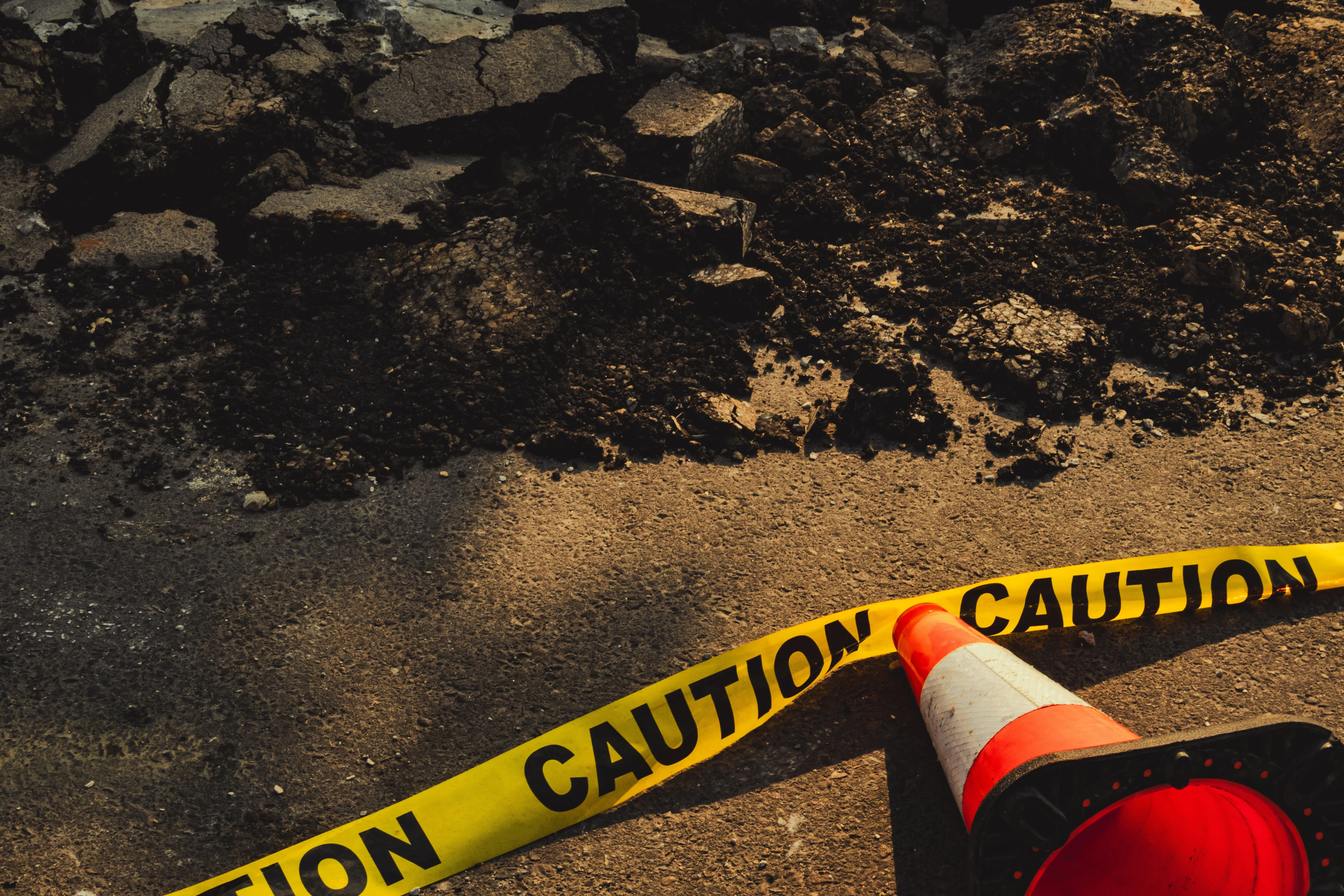 Deteriorated asphalt marked off with caution tape and a traffic cone